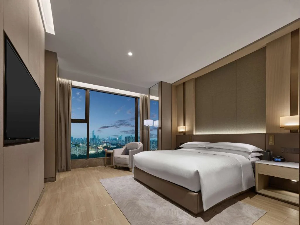 Modern hotel room with king bed and empty chair overlooking city skyline at dusk, quiet off-season travel retreat