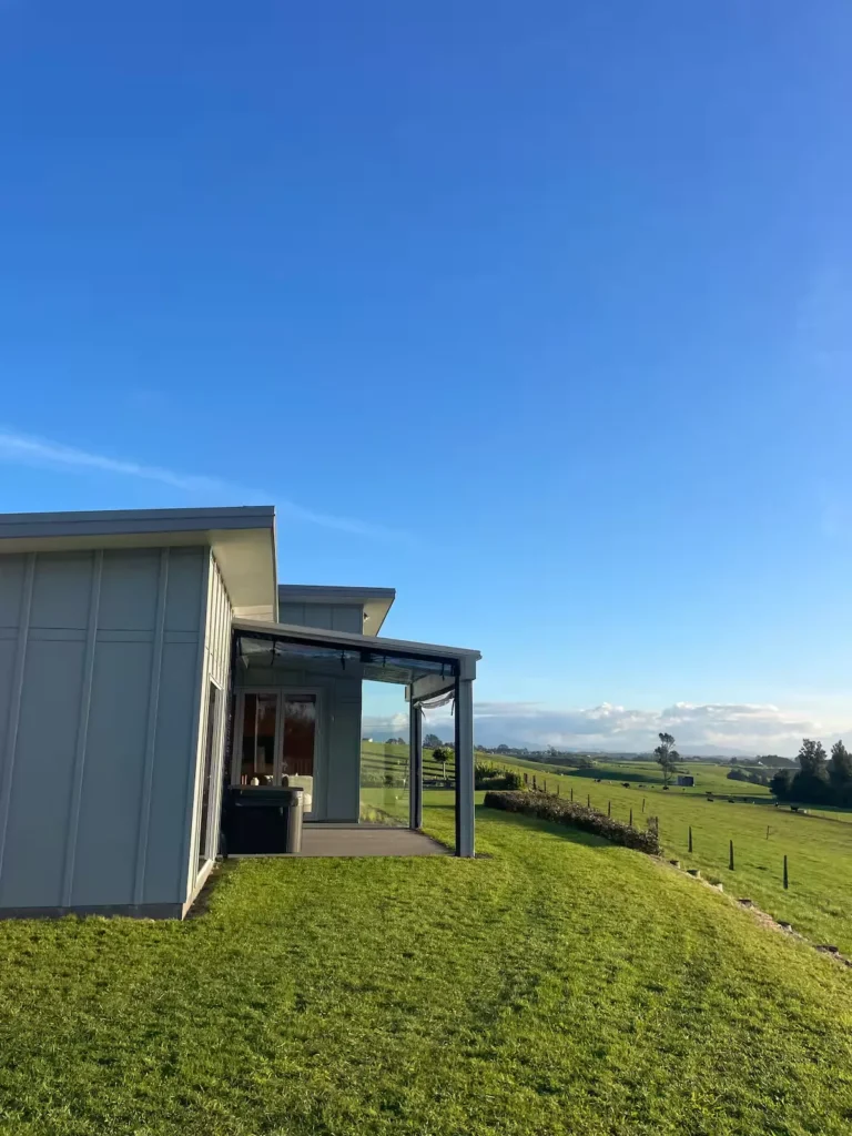 Modern hillside cabin overlooking empty green fields under a crisp blue sky in serene off-season calm.