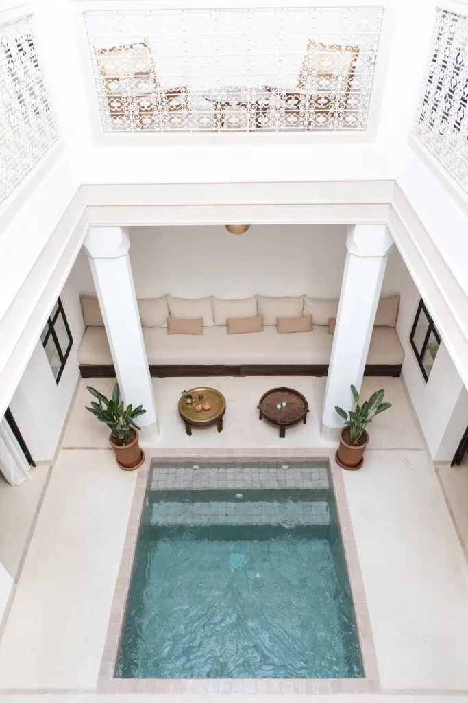 Empty Marrakech riad courtyard with central plunge pool, white stucco walls, ornate balcony and cozy off-season seating