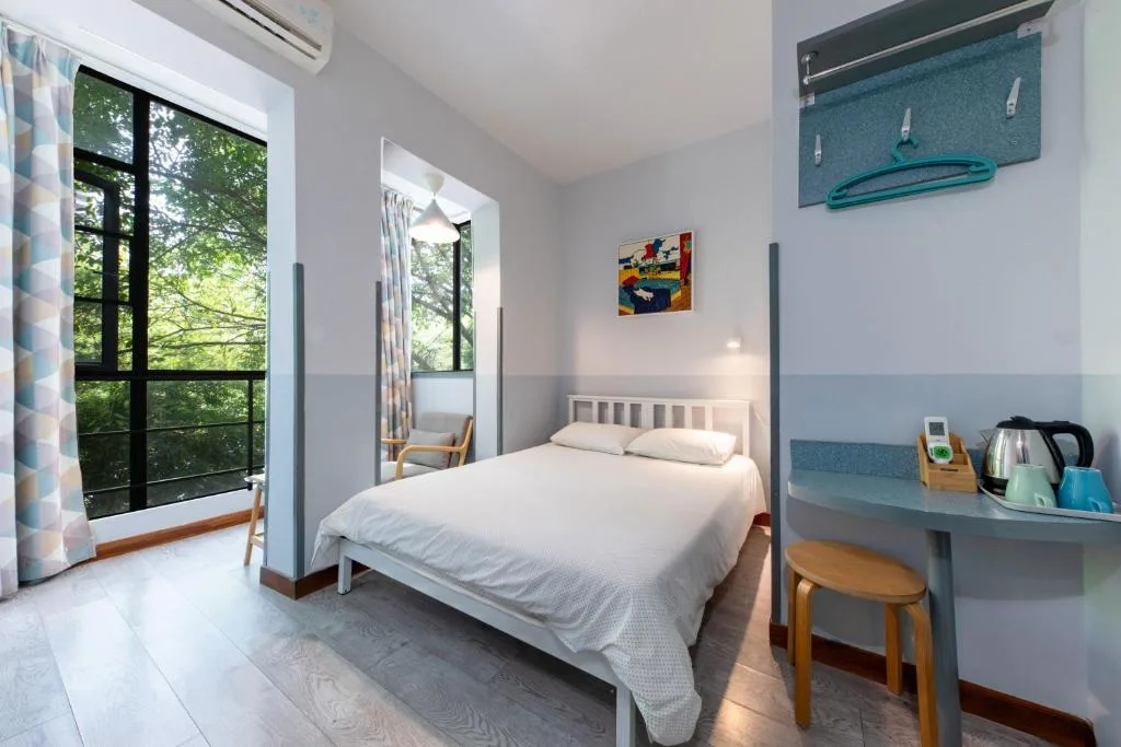 Off-season forest retreat room with white double bed, wide windows and lush greenery view for a peaceful travel getaway