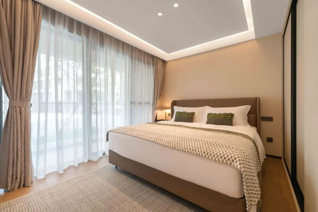 Spacious modern hotel bedroom with king bed, floor-to-ceiling windows and soft light, a serene off-season retreat.