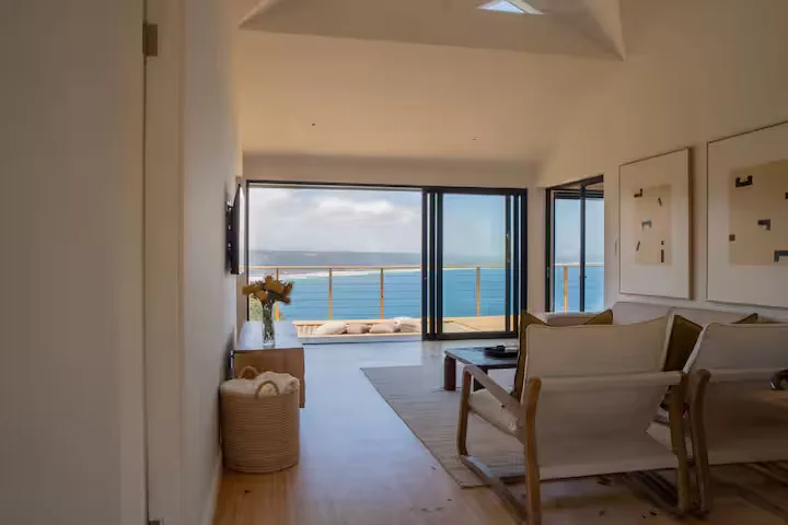 Empty coastal vacation rental living room with open glass doors to ocean-view balcony, highlighting tranquil off-season vibe.