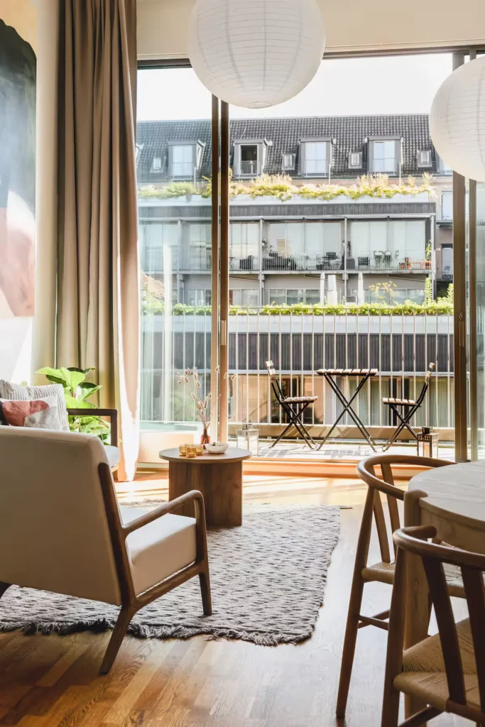 Sunny modern urban apartment living room with wooden furniture opening onto a quiet off-season balcony seating area.