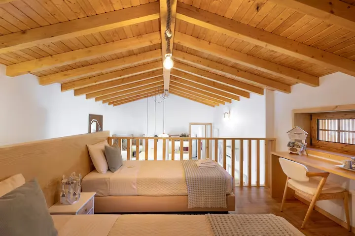 Cozy off-season attic loft bedroom in a wooden chalet with twin beds, exposed beams and workspace by a shuttered window