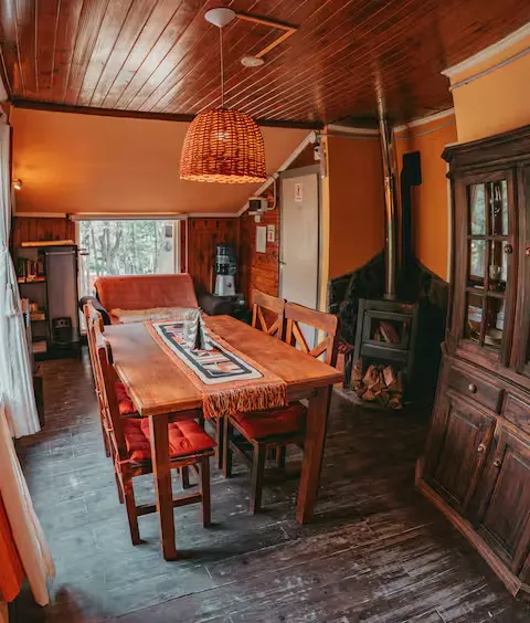 Cozy rustic wood cabin interior with dining table, wicker lamp and wood-burning stove in off-season gray light