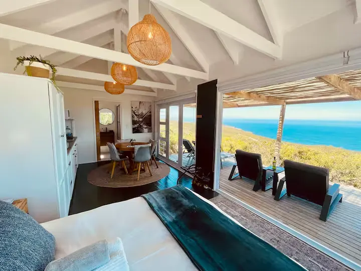 Off-season coastal cabin interior with wicker lights, dining area and deck chairs overlooking a tranquil open ocean view.