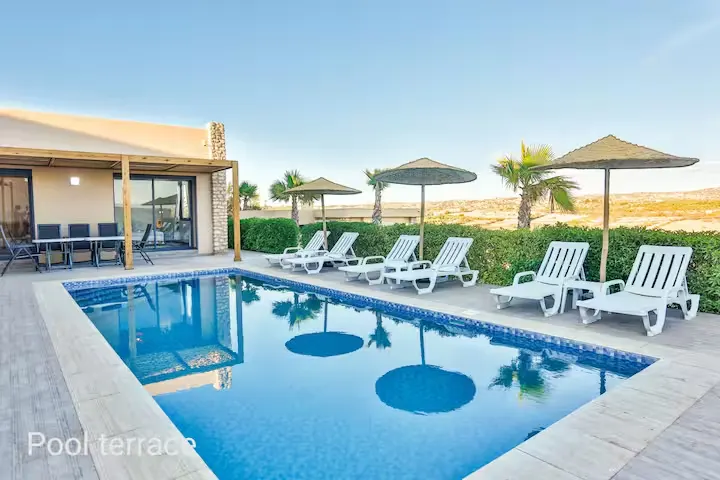 Empty sun loungers and straw umbrellas line a sunlit poolside terrace at a tranquil off-season retreat.