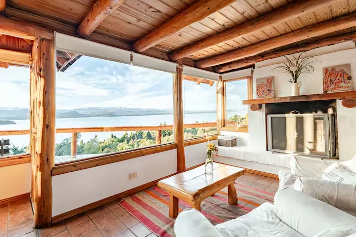 Cozy off-season lakeside cabin living room with wood-beamed ceilings, fireplace, and panoramic lake view under clear skies