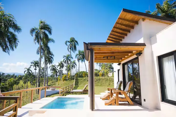 Empty tropical villa patio with pool and wooden lounge chairs under blue sky, off-season calm at this serene getaway.