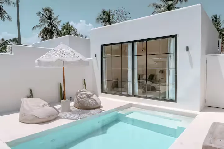 Minimalist white villa patio with private plunge pool, beanbag loungers and umbrella under palm trees in off-season calm.