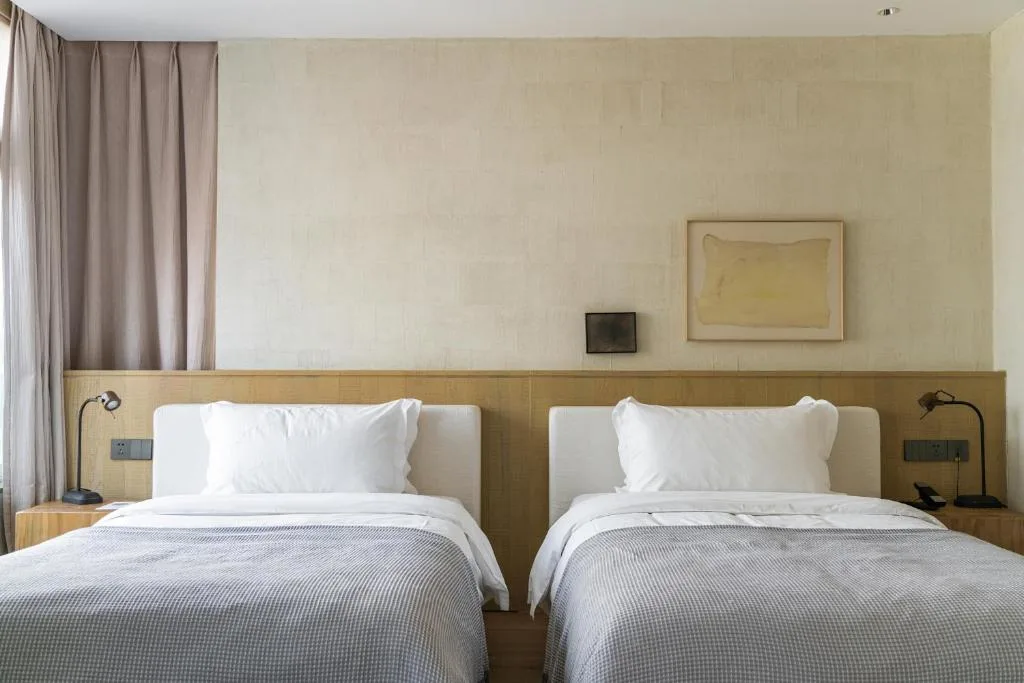 Minimalist twin hotel room in off-season: crisp white linens, soft gray throws, wooden accents and quiet bedside lamps.