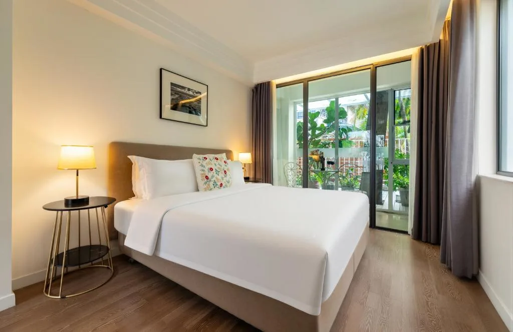 Serene modern hotel room with king bed and private balcony overlooking lush plants, ideal off-season travel retreat.