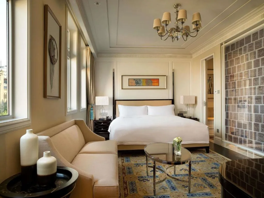 Empty luxury hotel room with king bed, sofa, chandelier and soft natural light, offering a quiet off-season travel retreat.