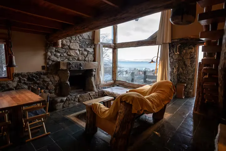 Rustic mountain cabin interior with stone fireplace and empty seating overlooking a misty lake in off-season calm