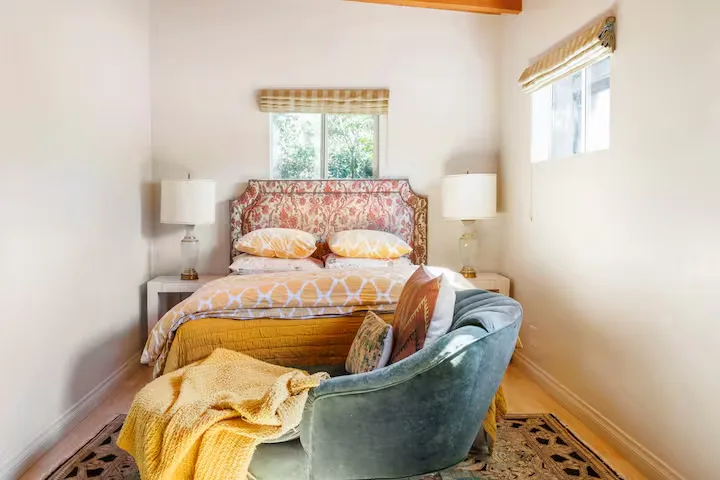 Cozy off-season travel rental bedroom with warm yellow bedding, patterned headboard and plush armchair in soft natural light