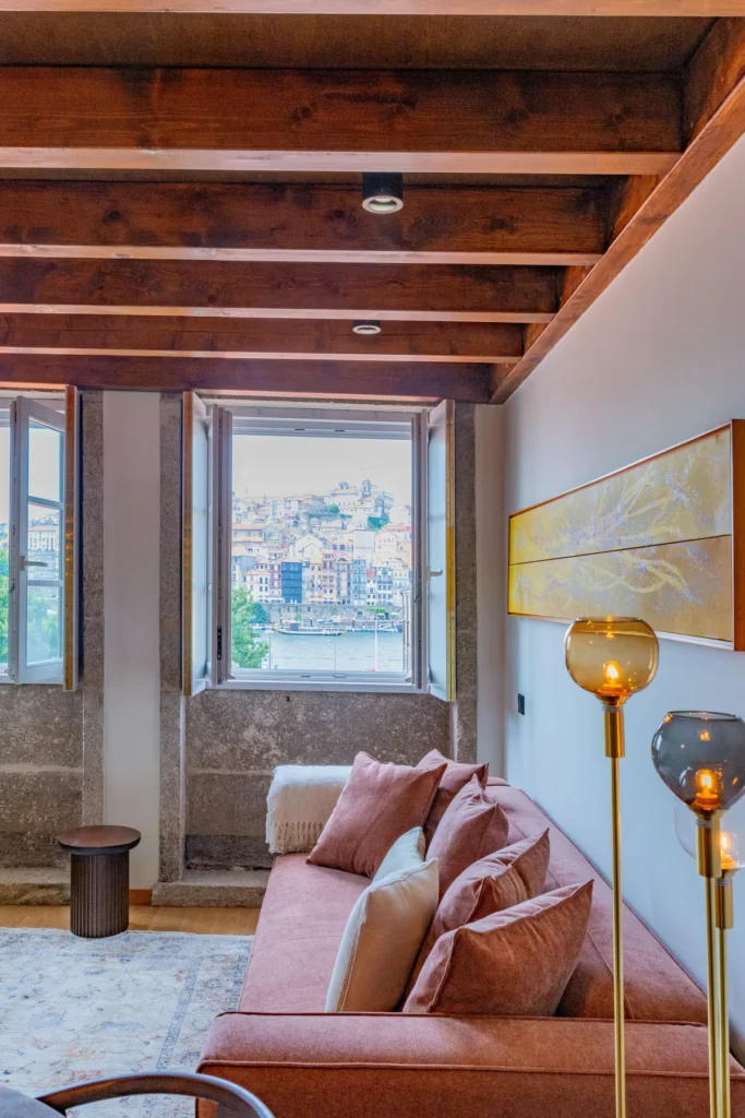 Cozy off-season Porto lounge with salmon sofa and open window overlooking the Douro River and pastel waterfront buildings.