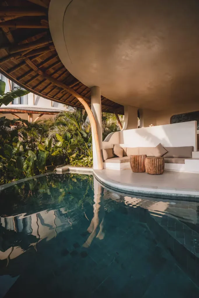 Empty tropical poolside resort lounge with thatched canopy, wooden stools and lush greenery in calm off-season escape