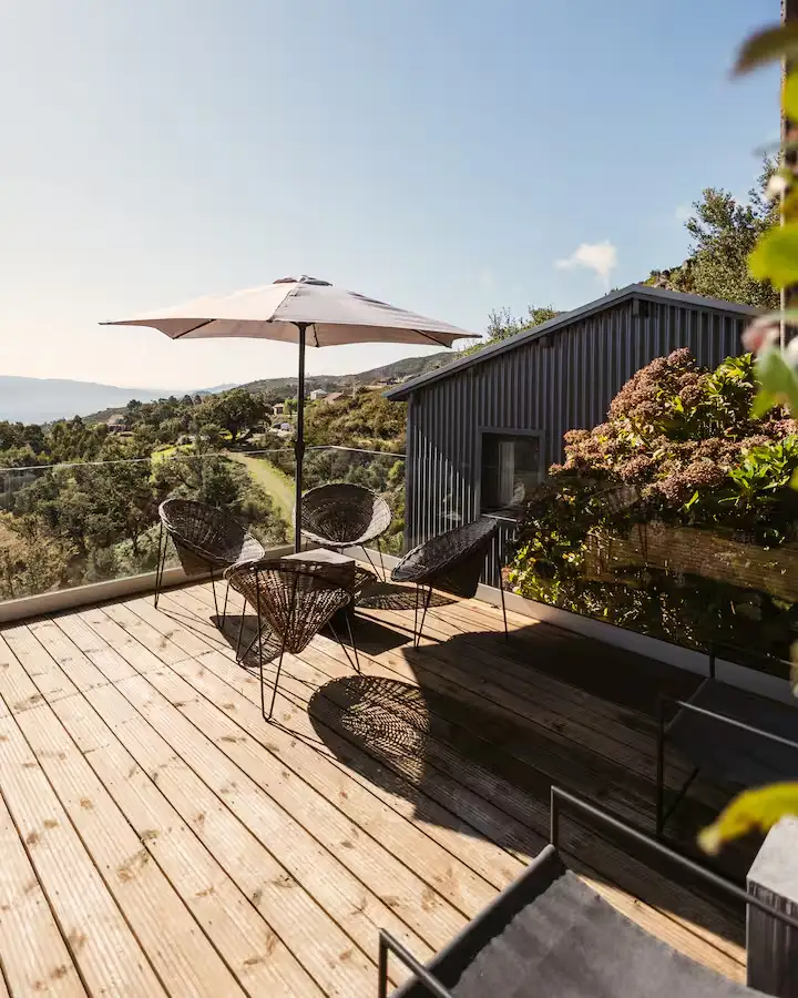 Quiet off-season travel terrace on wooden deck with wicker chairs, umbrella and serene hillside view