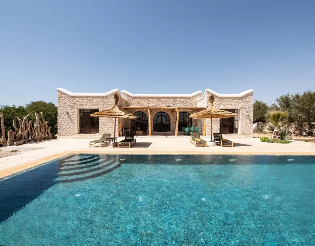 Stone villa poolside with sun loungers and thatched parasols under a clear sky, off-season serenity at a quiet travel retreat