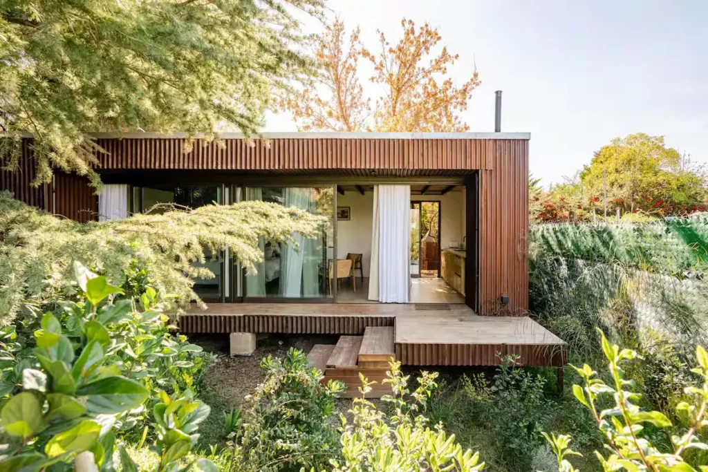Off-season wooden retreat with sliding glass doors opening to cozy interior, surrounded by autumn foliage and greenery.