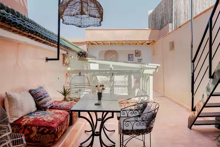 Empty off-season travel rooftop terrace with pastel walls, wrought-iron table, vibrant cushions and rattan pendant light.