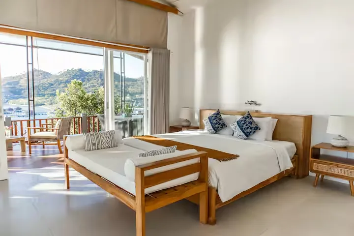 Sunlit minimalist hotel suite with empty balcony overlooking tranquil waterfront hills in a peaceful off-season retreat.