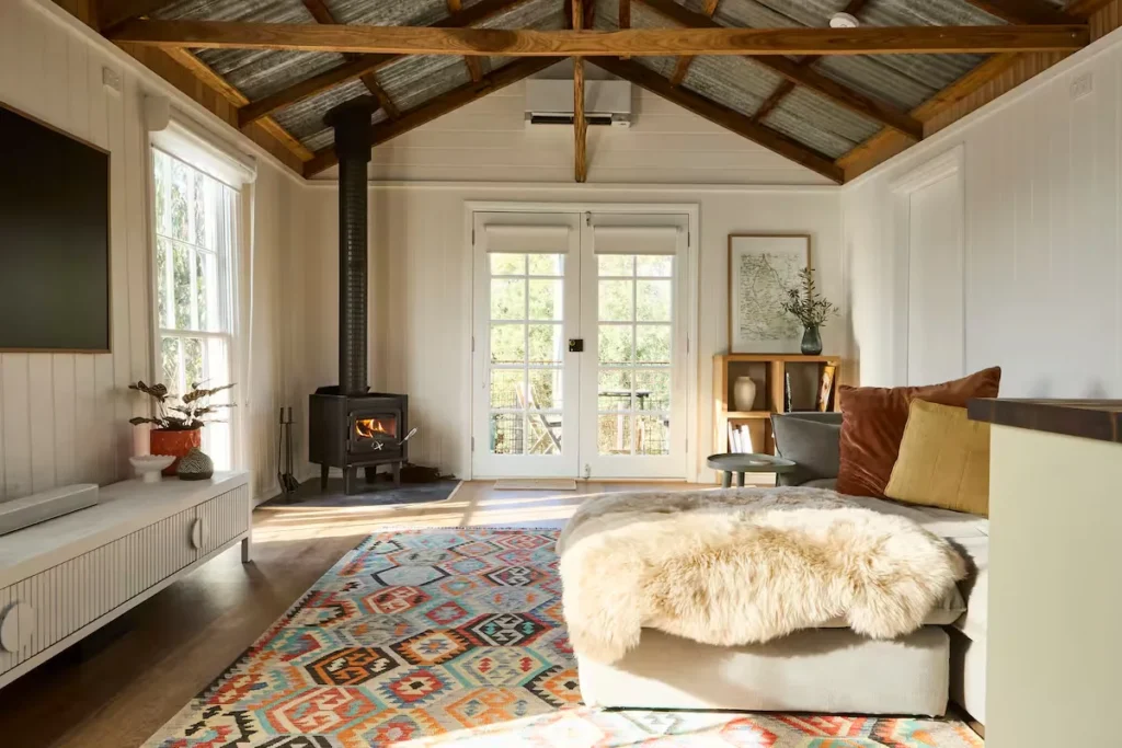 Cozy sunlit cabin interior with wood-burning stove and fluffy sheepskin throw, an idyllic off-season travel retreat.