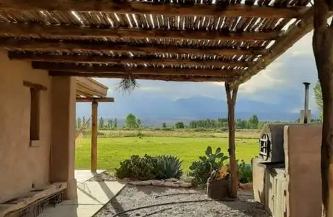 Rustic adobe terrace with wooden pergola overlooking empty green fields and distant mountains in off-season travel retreat.