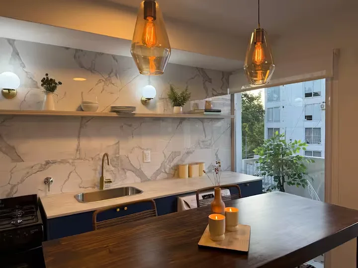 Cozy off-season vacation rental kitchen with marble backsplash, amber pendant lights, scented candles and quiet balcony view.