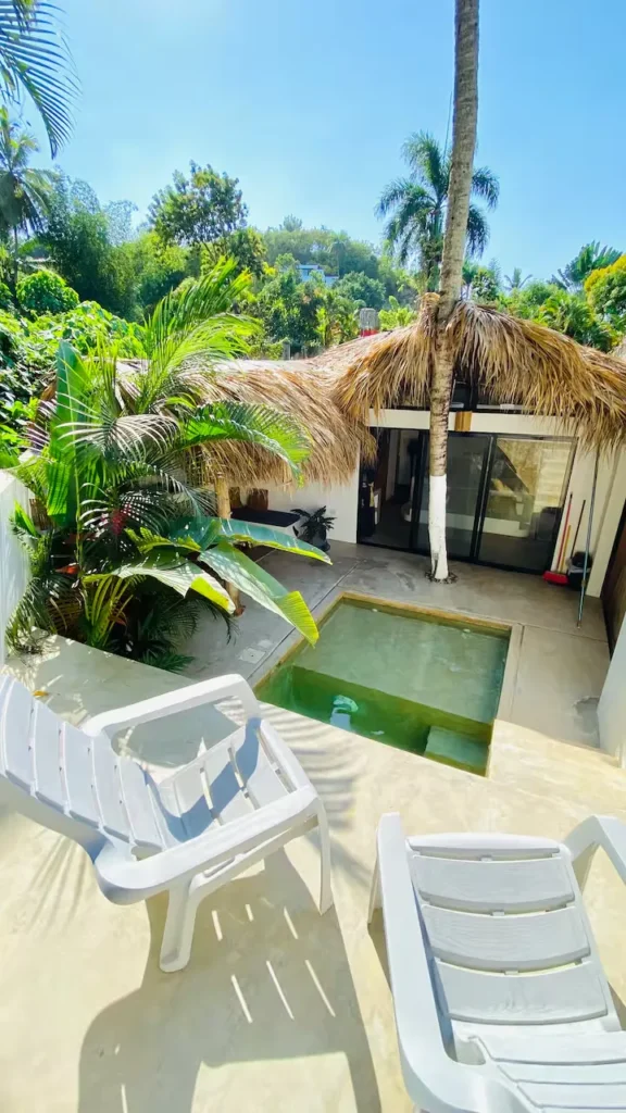 Off-season tropical villa courtyard with private plunge pool, empty white loungers and lush palm foliage under bright sun