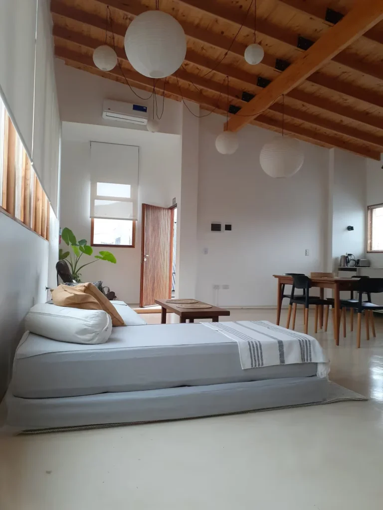 Bright minimalist loft retreat with wooden beams, paper lanterns and a low sofa-bed, offering a serene off-season getaway.