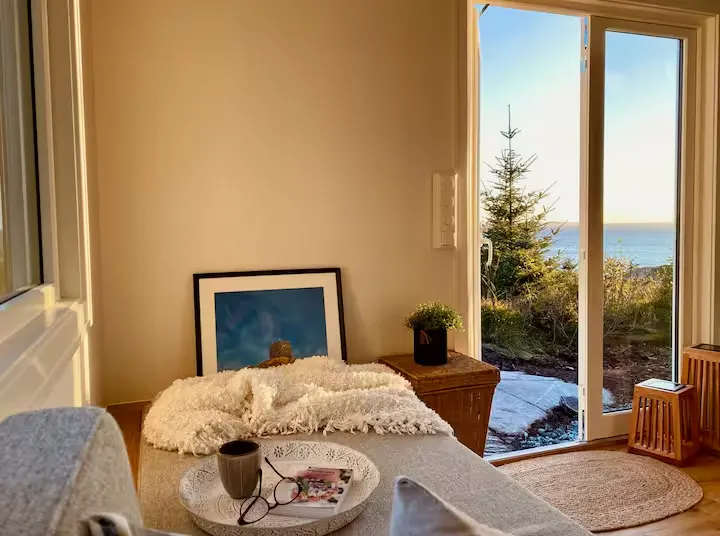 Cozy off-season oceanfront cabin lounge with plush throw and coffee, open sliding door to a serene seaside view