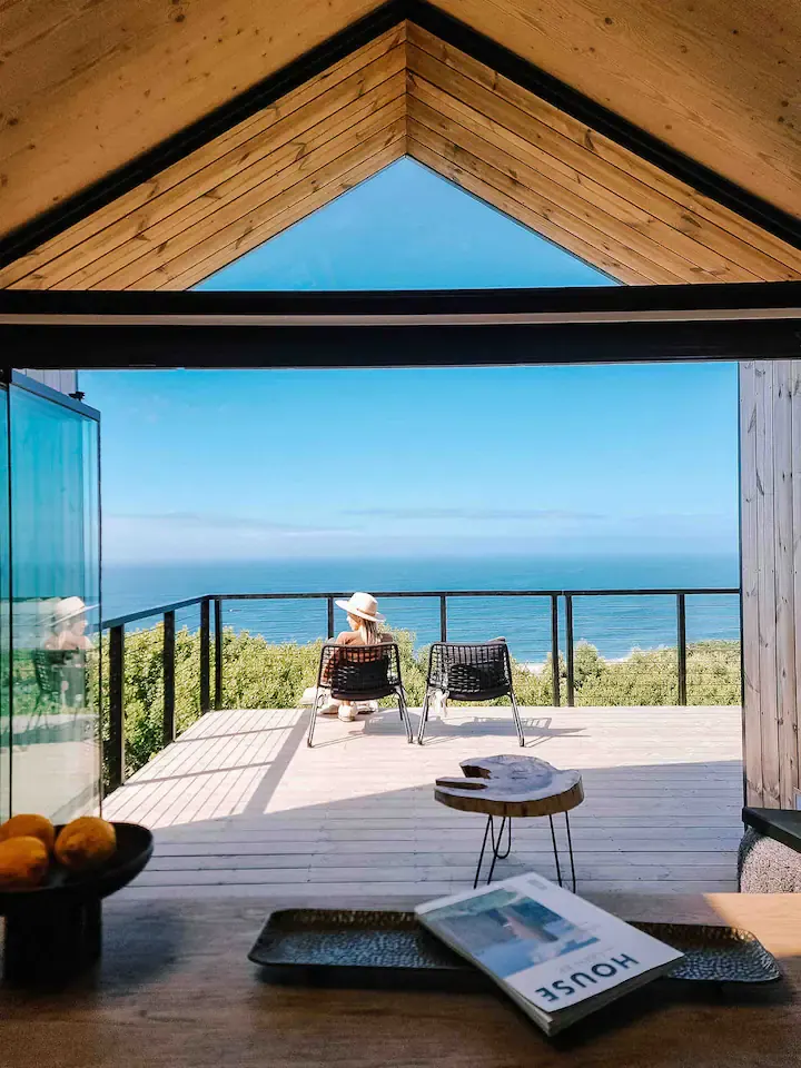 Quiet off-season beach retreat with lone traveler in sun hat on wooden deck overlooking calm blue ocean horizon.