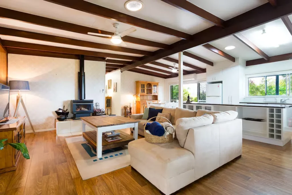 Cozy off-season holiday rental interior with wood-beamed ceiling, fireplace, plush sofa and open-plan kitchen