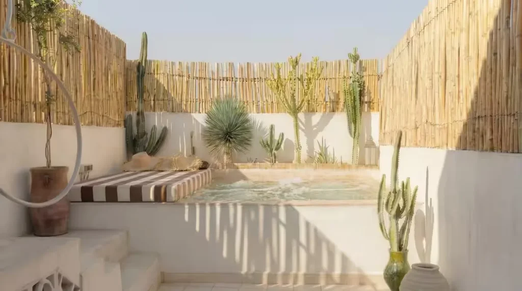 Sunlit rooftop plunge pool with striped lounge cushion, bamboo fence and potted cacti in a quiet off-season retreat