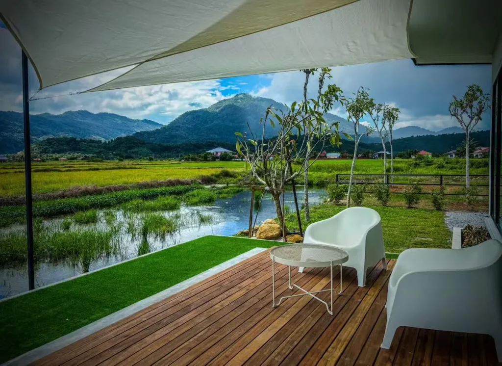 Wooden deck with white chairs under canopy overlooking rice paddies and misty green mountains for tranquil off-season travel.