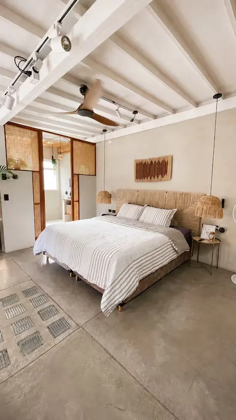 Minimalist boutique hotel bedroom with rattan headboard, concrete floor and warm lighting for a peaceful off-season stay.