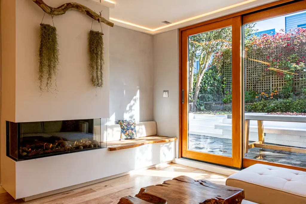 Cozy vacation rental living room with built-in fireplace and garden patio view through glass doors, off-season calm.