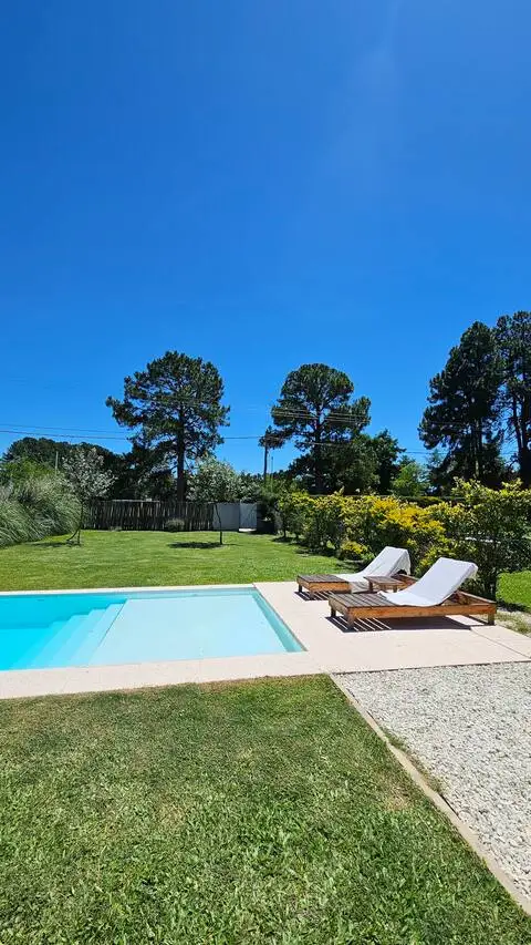 Off-season poolside retreat with empty sun loungers on a green lawn under clear blue sky, perfect for a tranquil getaway.