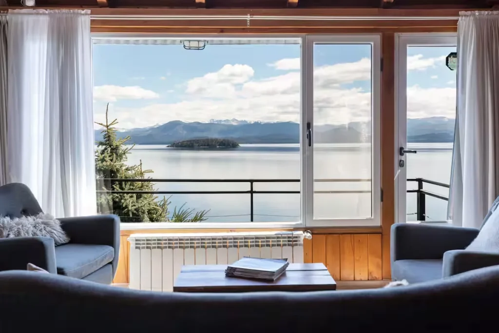 Off-season lakeside cabin with empty seating overlooking tranquil lake, island and distant mountain peaks under cloudy sky