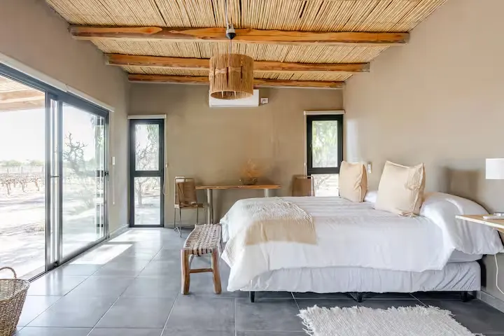 Spacious lodge bedroom with wooden-beamed ceiling and sliding glass doors overlooking empty landscape, off-season calm