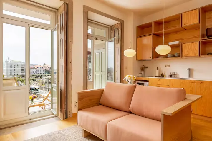 Cozy city apartment interior with wooden kitchen, pastel sofa and open balcony overlooking quiet rooftops in off-season calm.