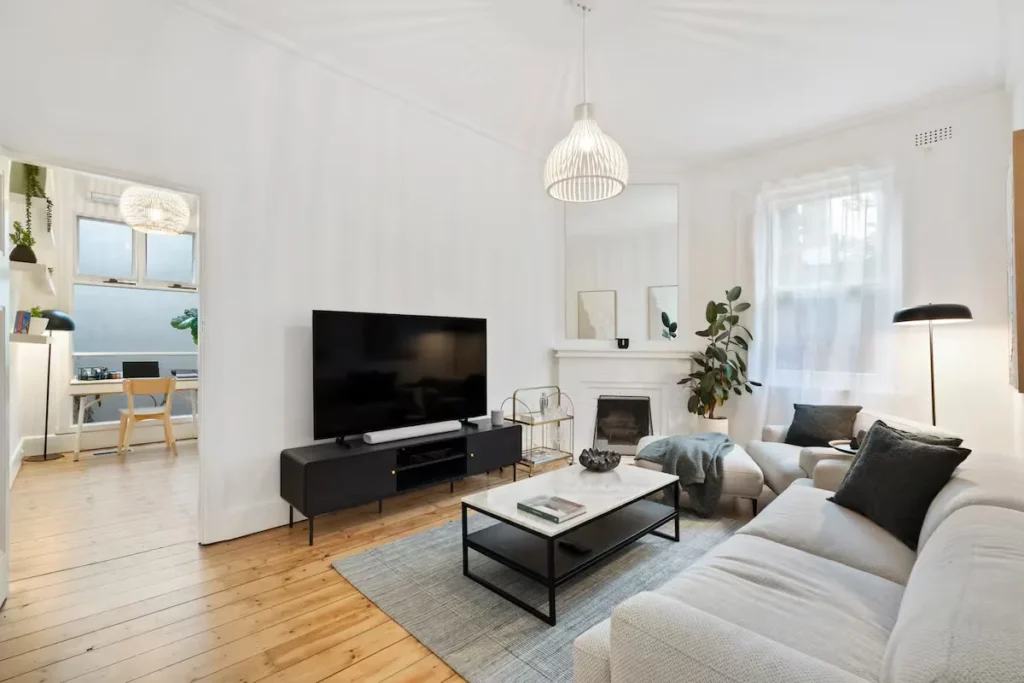 Cozy off-season city apartment living room rental with modern minimal decor, fireplace, large sofa and bright work nook.