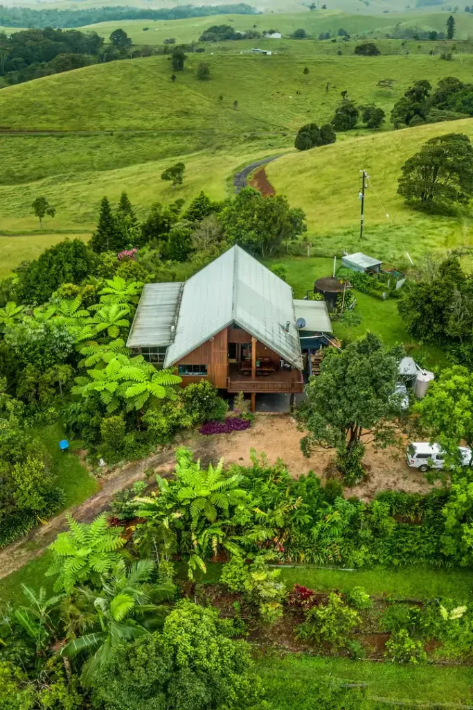 Elevated view of a secluded wooden farmhouse in lush green hills, off-season travel calm at a misty rural retreat.