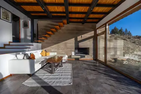 Cozy travel cabin interior in off-season mountain retreat with wood beams and panoramic glass wall overlooking quiet slopes