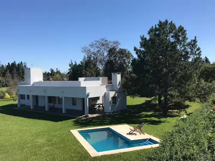 Modern white villa and pool on empty green lawn under clear sky, lounge chair and picnic table in off-season retreat
