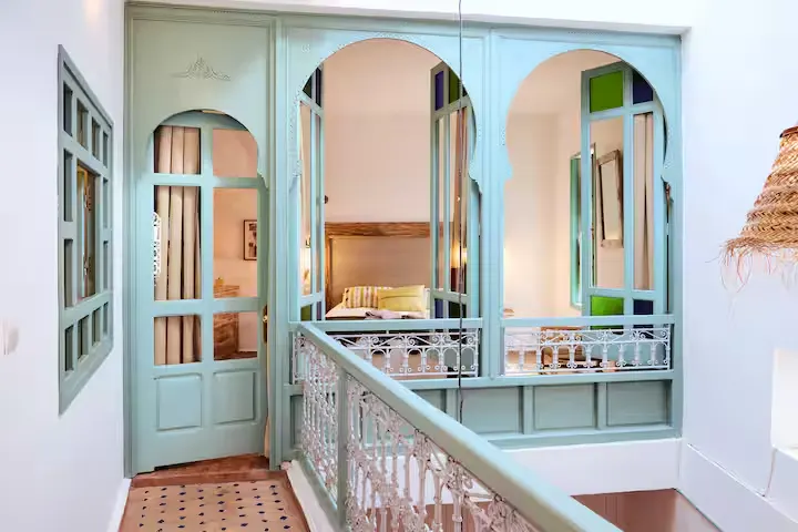 Sunlit mint-green arches and intricate railing in a quiet boutique guesthouse hallway, evoking an off-season travel vibe.