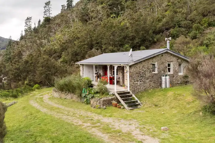 Off-season travel scene at a stone cottage nestled in green hills with an empty dirt path and quiet, muted atmosphere.