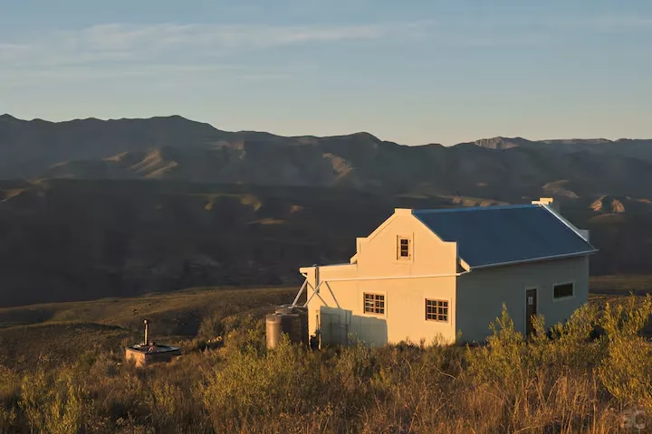 Golden-hour glow on a remote hillside cottage overlooking an empty mountain valley, evoking off-season travel serenity.