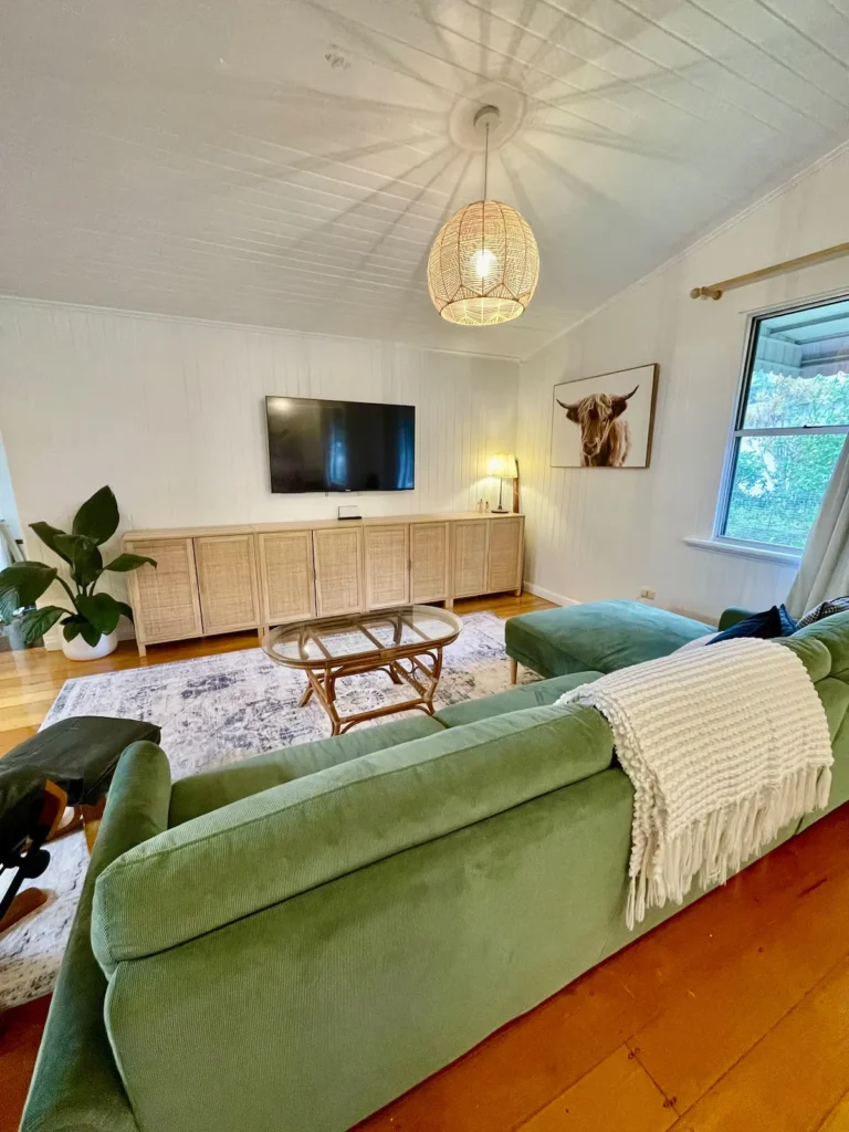 Cozy off-season vacation rental living room with plush green sofa, rattan cabinets, soft lighting and garden view.
